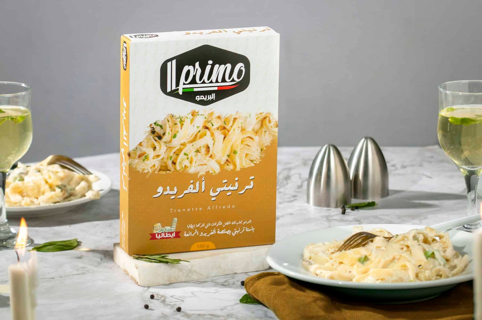 عبوة مكرونة ترنيتي ألفردو (Trenette Alfredo) من Il Primo بوزن 160 جرام، بجانب طبق مكرونة بصوص الكريمة البيضاء.