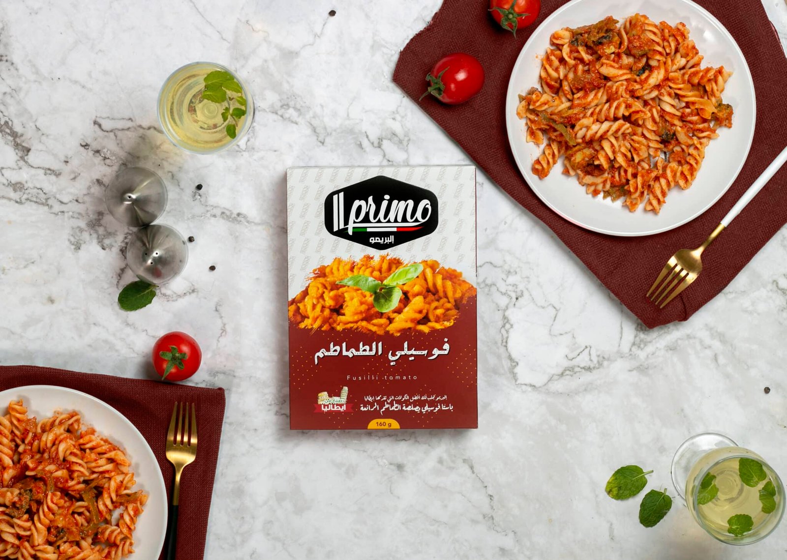 عبوة مكرونة فوسيلي بالطماطم (Fusilli Tomato) من Il Primo بوزن 160 جرام، مع طبقين من المكرونة بالصلصة الحمراء وطماطم طازجة.